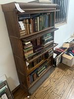 Front view of the tall wooden bookcase filled with various old books. The glass doors covering each shelf are visible and appear misaligned or not closing properly.