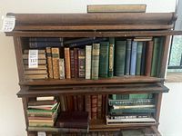Wooden barrister-style bookcase filled with antique books of various sizes, colors and bindings