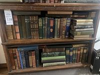 Two-tier wooden shelves holding approximately 30 decorative cloth-bound books in assorted colors
