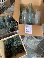 Three boxes containing a variety of antique glass bottles in different sizes and colors including clear, green, and brown hues.
