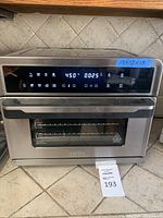 Full front view of Aria air fryer showing digital touch control panel, glass door with handle, and dimensions sticker 15x18x15 inches.