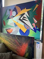 Wide view of both abstract paintings showing geometric colorful painting above and textured dark burst painting below.