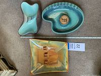 All three ceramic Art Deco style ashtrays on carpet background with measuring tape