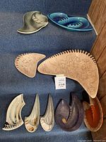 Eight ceramic art deco ashtrays and decorative plates in various shapes and colors arranged on blue carpeted stairs.