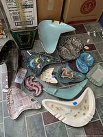 Group view of eleven ashtrays in various shapes and colors on tiled floor