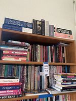 Wooden bookshelf filled with multiple rows of books in various sizes and colors. Large reference books on top including English language references and encyclopedias.