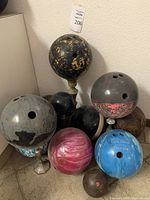 Photo showing multiple bowling balls of various colors and patterns, including marbled black and gold, blue, pink and white, brown, and solid colors.