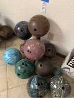 Full view of 11 bowling balls with various colors and patterns arranged on a tiled floor