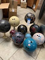 Photo of 11 bowling balls of various colors and patterns arranged on tile floor, including black, yellow speckled, marbled, and blue balls.