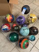 Top view showing all 12 bowling balls arranged on the floor in assorted colors and patterns including rainbow swirl, marbled, solid colors, and striped balls.
