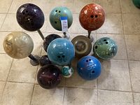 Top-down view of 11 bowling balls of various brands, colors, and some personalized engravings placed on tiled floor.