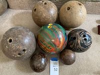 Top view showing seven bowling balls of different styles and sizes including wooden and plastic balls, arranged on carpeted floor.