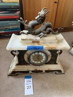 Front view showing white and orange-veined marble base, round enamel and brass dial, metal floral appliques, and dragon figurine topper