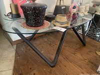 Side angle showing the triangular wooden base supporting an oval glass top, placed on a hardwood floor with items on top for scale.