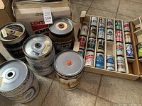 Overview of several keg-shaped empty beer cans and a box of smaller empty beer cans from various international breweries.