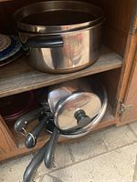Photo of medium and large stainless steel cookware including pots and saucepans with lids and black handles inside a cabinet.
