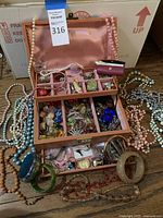 Overview of open pink jewelry box with assorted necklaces, bracelets, brooches and earrings spread around