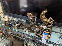 Four Yona Ceramics statues displayed on a glass and metal piece of furniture beneath a TV: three dancers and one horse statue.