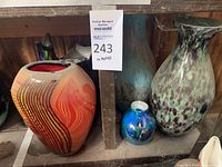 Wide view showing six decorative glass flower vases with varied colors and shapes on wooden shelving.