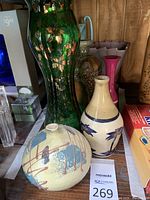 Photo showing the round pottery vase with abstract design and the beige ceramic vase with blue bird motifs, along with the large green glass vase and pink ceramic vase in background.