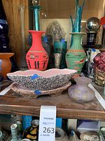 Overview of shelf with woven vases, speckled bowl, tray, marbled glass vase, mirrored decanter, black carved vase and teal cylinder vase