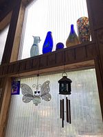 Wide view of the glass vases displayed on a wooden shelf with two hanging decorative items visible below.