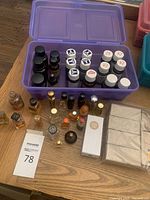 Overview of lot showing a purple plastic container holding multiple small brown and clear bottles with black and white caps. Several small glass bottles and boxed product placed on table around container.