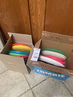 Two cardboard boxes filled with assorted colored plastic frisbees stacked vertically.