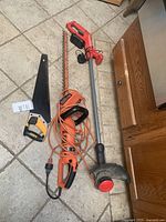 Lot showing manual hand saw, Dewalt reciprocating saw, Black & Decker electric hedge trimmer, and Craftsman cordless hedge trimmer lying on tiled floor