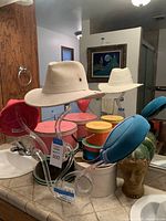 Two hats on clear acrylic hat stand with several vintage hat boxes in the background on a bathroom counter near a mirror.
