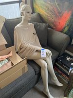 Full view of seated mannequin on loveseat with cardboard box of loose parts to left