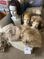 White plastic mannequin head wearing a short brown wig alongside two ceramic heads and pile of loose wigs