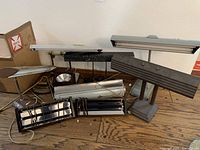 Overview of all metal desktop lamps and light fixtures grouped together on a wooden floor, showing various designs and colors mainly in silver, gray, and black.