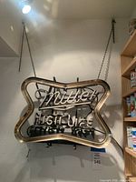 Front view of the Miller High Life neon sign unlit, hanging on wall by chains