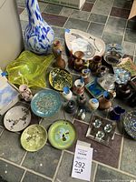 Wide view showing collection of miniature vases, decorative plates, and glass decor pieces on tiled floor.