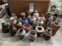 Collection of 21 miniature pottery pieces in various shapes, sizes, and colors arranged on floor with cardboard box background