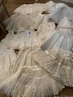 Photo showing spread of white, cream, and beige petticoats and underskirts with lace and gathered layers laid on floor.
