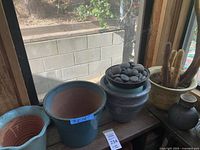 Wide view of various planters including a large blue glazed planter marked 9 x 12 inches, smaller pots, black decorative rocks in a bowl, and cactus plants in cream swirl pots.