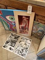Overall view of three framed artworks and two loose comic art boards on tiled floor