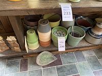 Shelf display of stackable pottery planters in various colors and shapes with a ceramic leaf-shaped dish on floor.