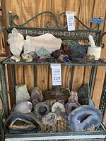 Two-tier decorative metal stand displaying various mineral specimens including quartz clusters, slab, geodes and crystals