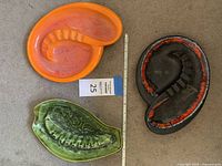 Three ashtrays on carpet: orange Royal Haeger, black and red Royal Haeger, and green Cal Styse USA ashtray. Ruler for scale.