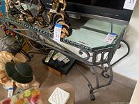 Full view of the metal framed side table with glass top among surrounding items for sale.