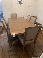 Full view of the rectangular wooden dining table surrounded by six beige upholstered chairs in a room with hardwood flooring.