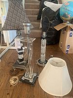 Overall view of three acrylic tabletop lamps with several lamp shades around them on wooden floor