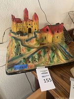 Front view of ceramic village scene lamp showing castle and house with a color label indicating dimensions 11 x 15 x 10 inches.