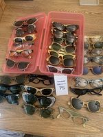 Multiple pairs of vintage glasses and sunglasses arranged in pink storage bin and on wood floor
