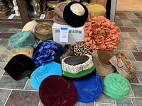 Photo showing entire collection of 15 vintage ladies hats in multiple colors, materials, and styles arranged on tiled floor.