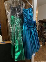 Two vintage ladies prom party dresses hanging side by side. One is a metallic green with a black bodice and the other is a bright shiny blue strapless dress.