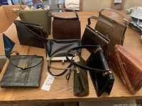 Wide shot showing all 10 vintage purses and clutches spread on a wooden surface, in black, brown and green tones, various styles and materials.